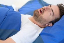 Man snoring and showing one possible sleep apnea symptom